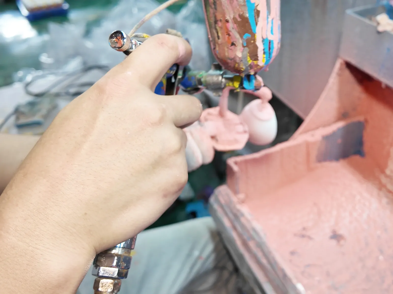The operator uses a semi-automatic spray gun for coloring, with an exhaust fan in front to remove excess fumes.
